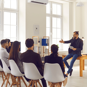 Mitarbeiter sitzen in einem Workshop mit einem Workshopleiter, der über Stressbewältigungstechniken spricht.