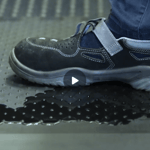 Arbeitsschuh tritt auf eine ergonomische Arbeitsplatzmatte mit rutschhemmender Oberfläche, auf der Öl verschüttet ist.