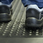 Arbeitsschuhe auf einer ergonomischen Gummimatte mit strukturierter Oberfläche, die Öl und Metallspäne sicher auffängt und die Rutschsicherheit gewährleistet.