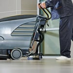 Reinigungskraft fährt eine Bodenreinigungsmaschine, um Verschmutzungen zu entfernen und Rutschgefahr im Arbeitsbereich zu minimieren.