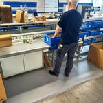 Produktionsmitarbeiter steht auf einer ergonomischen Arbeitsplatzmatte und höhenverstellbaren Kommissionierungstisch