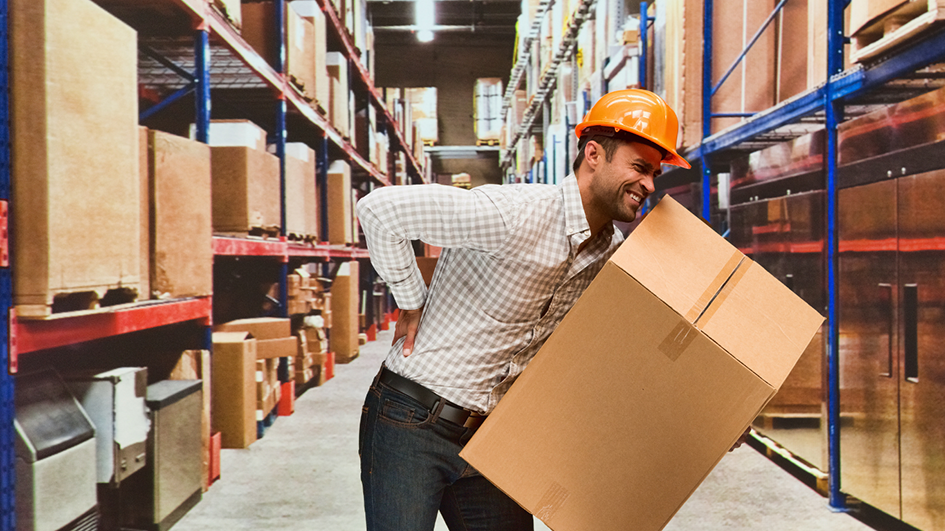 Ein Mann sitzt im Lager und hält sich den Rücken. Sein Arbeitsplatz ist nicht ergonomisch eingerichtet.