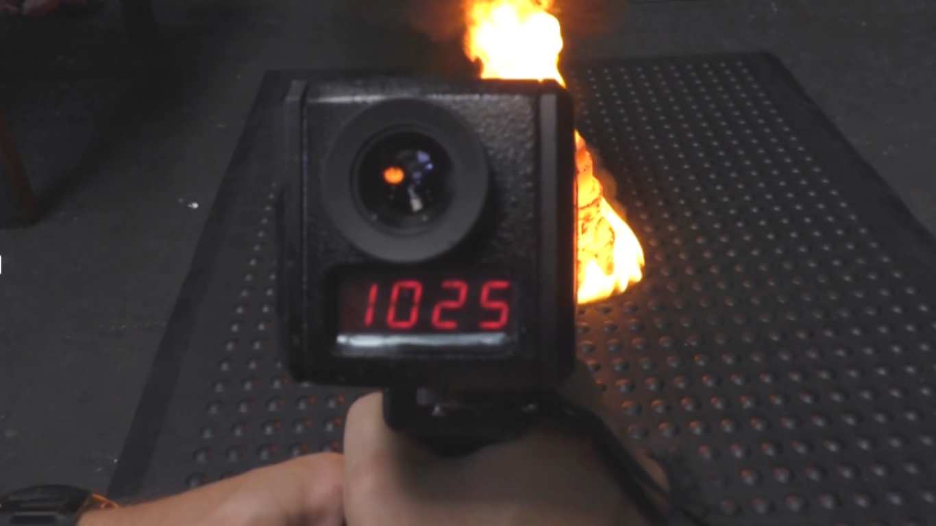 Eine Temperaturmessung zeigt 1025 °C an, während eine Flamme auf einer Arbeitsplatzmatte brennt. Der Test demonstriert die hohe Hitzebeständigkeit der ERGOLASTEC OIL Matte von KRAIBURG MATTING SYSTEMS – entwickelt für den täglichen Einsatz in Werkstätten und Produktionsumgebungen.