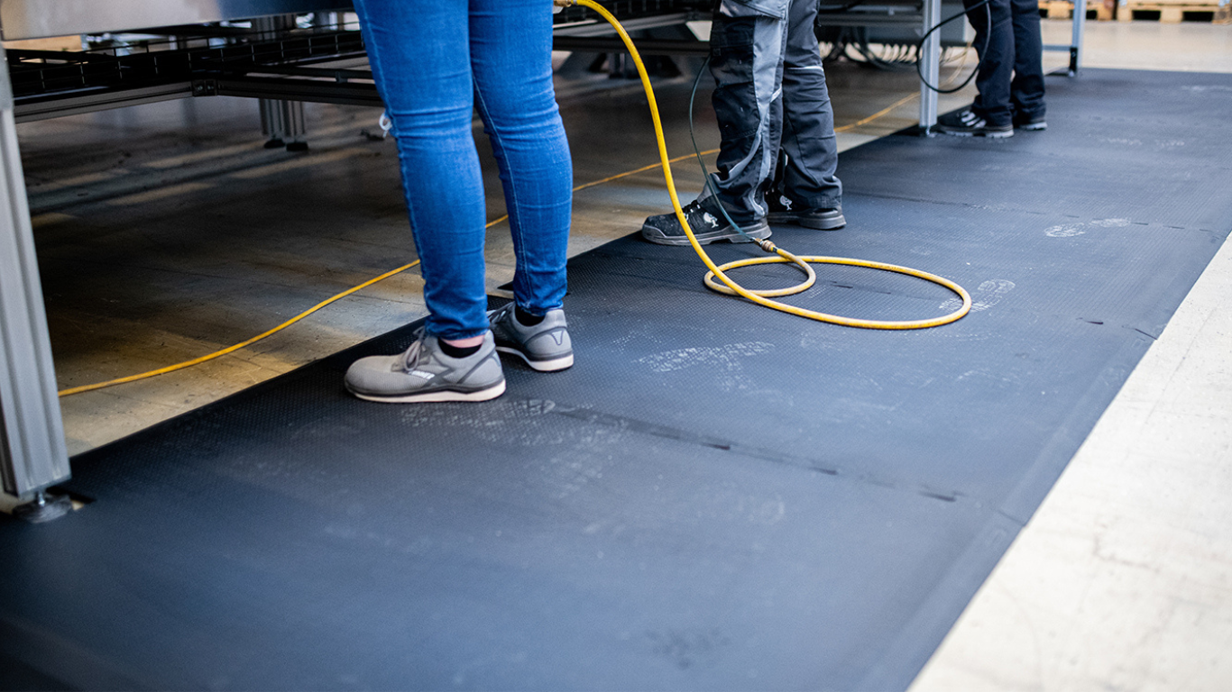 Mitarbeitende stehen auf einer Anti-Ermüdungsmatte an einem Produktionsarbeitsplatz – ergonomische Bodenlösung für langes Stehen